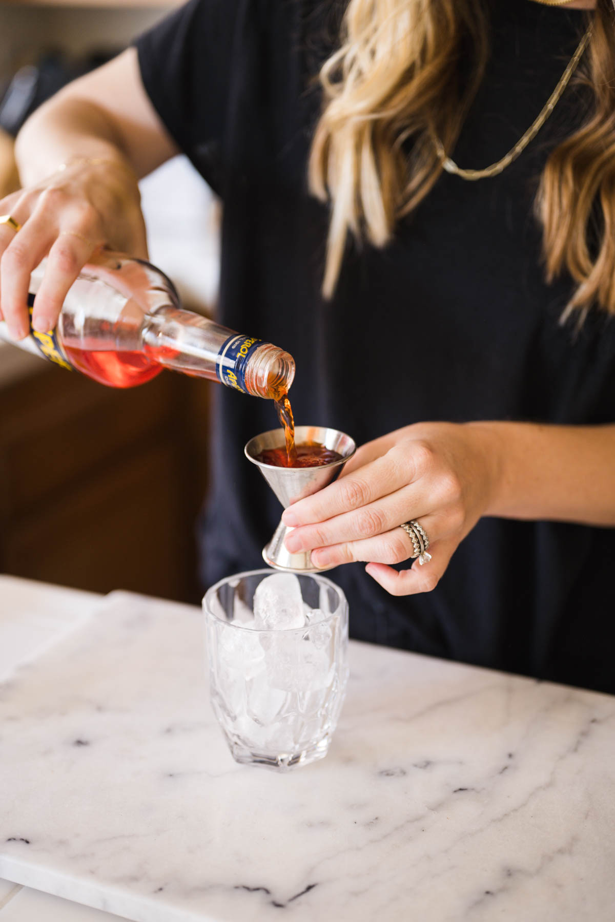 Woman measuring Aperol in a jigger next to a cocktail glass.