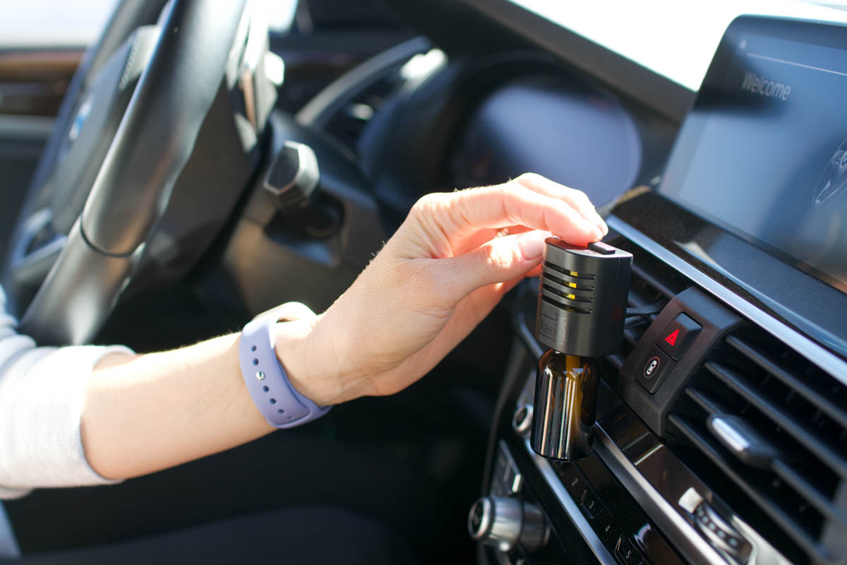An essential oil diffuser for the car being turned on by a woman's hand.