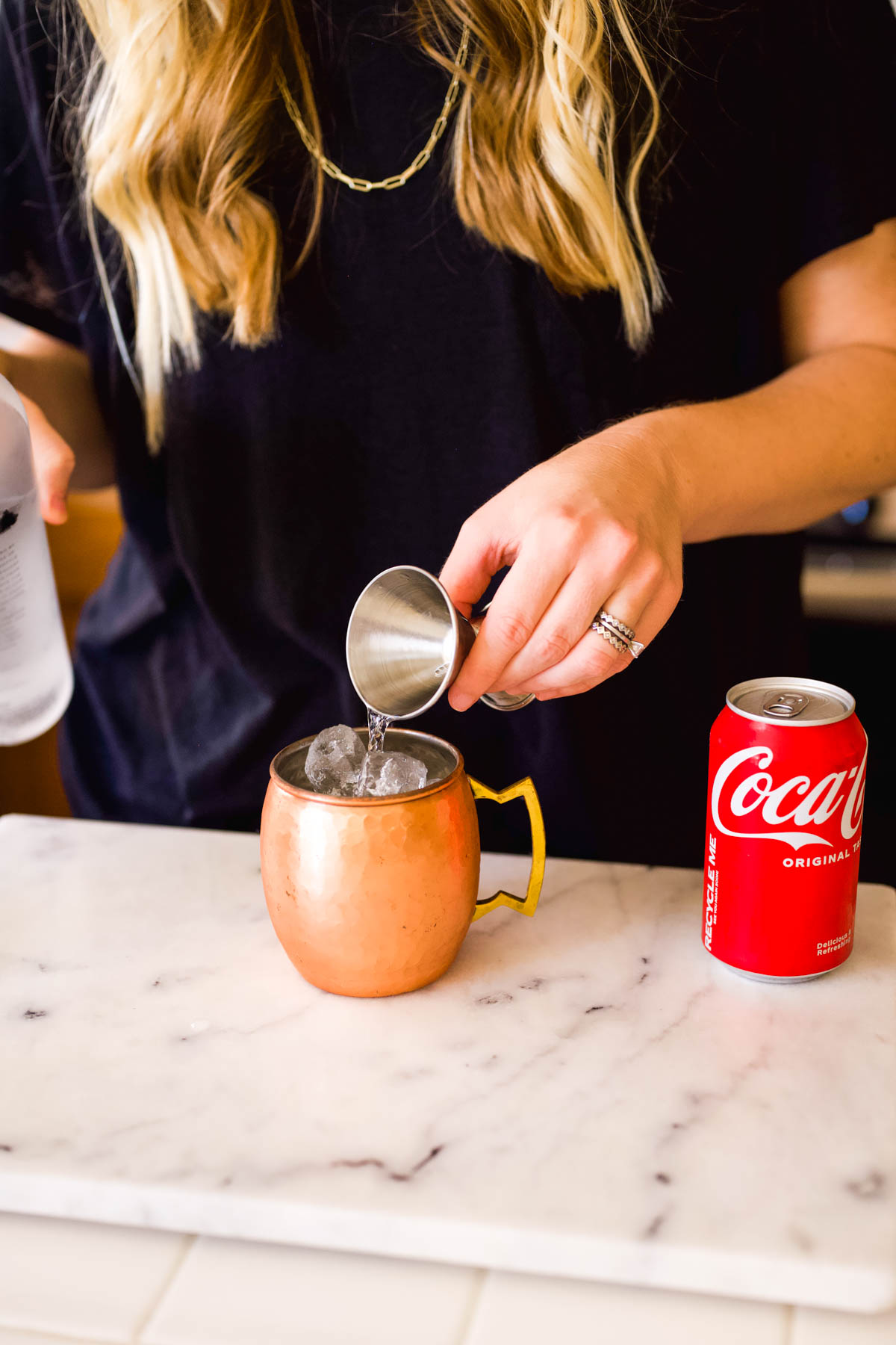 Woman pouring Coke into a copper mug with a jigger.