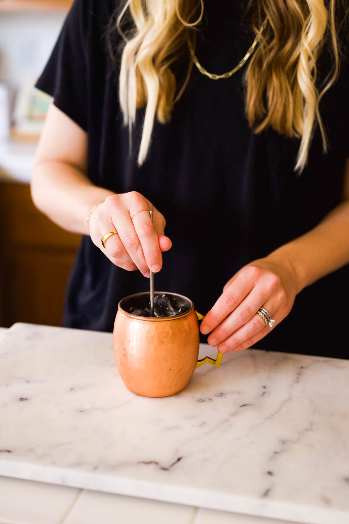 Woman using a bar spoon to stir a cocktail in a copper mug.