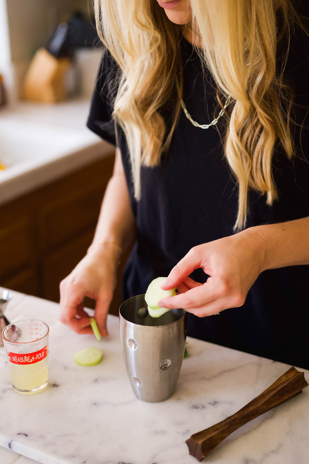 Woman adding cucumber slices to a cocktail shaker.