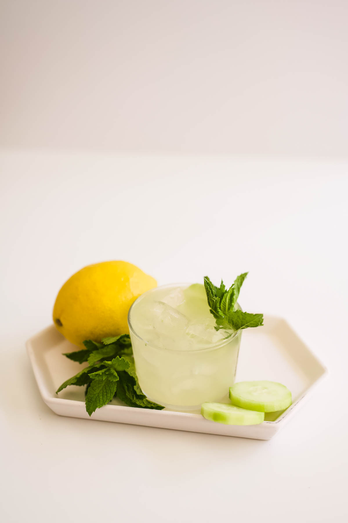 Cocktail on a small tray with lemon, mint and cucumber slices.