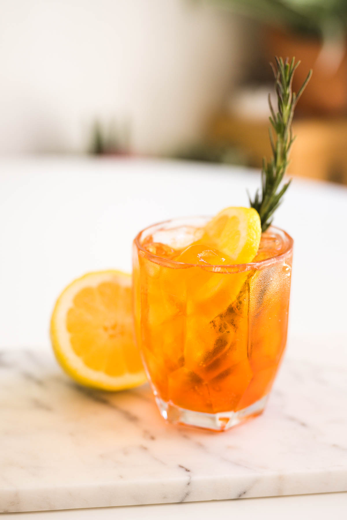 An Aperol and Soda cocktail in a cocktail glass with lemon wedge and rosemary sprig. 