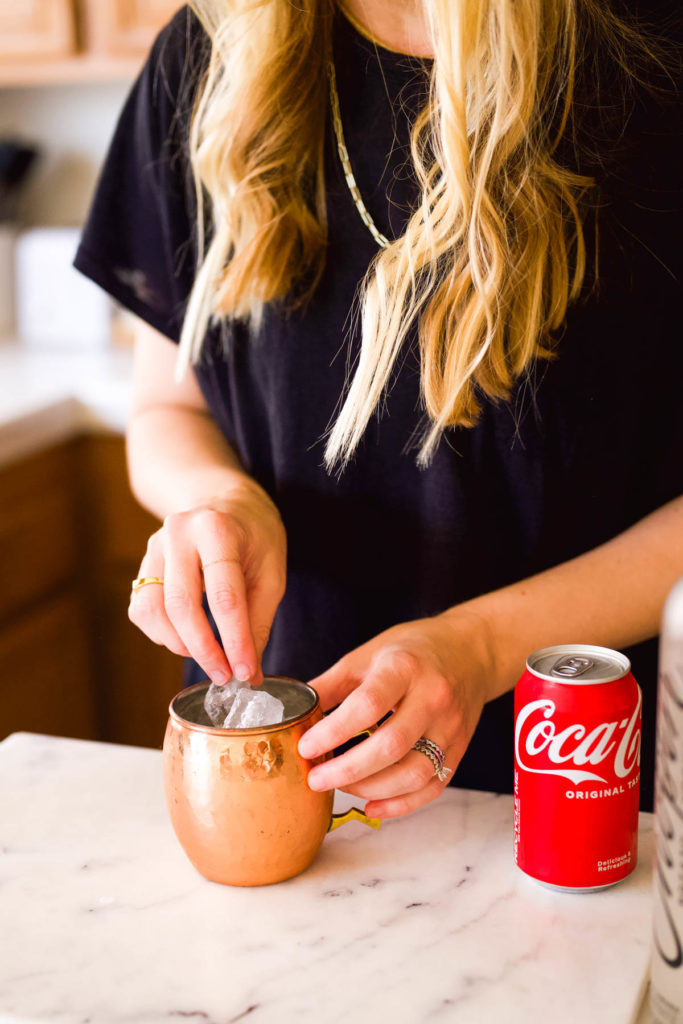 Woman adding ice to a copper Moscow Mule mug.
