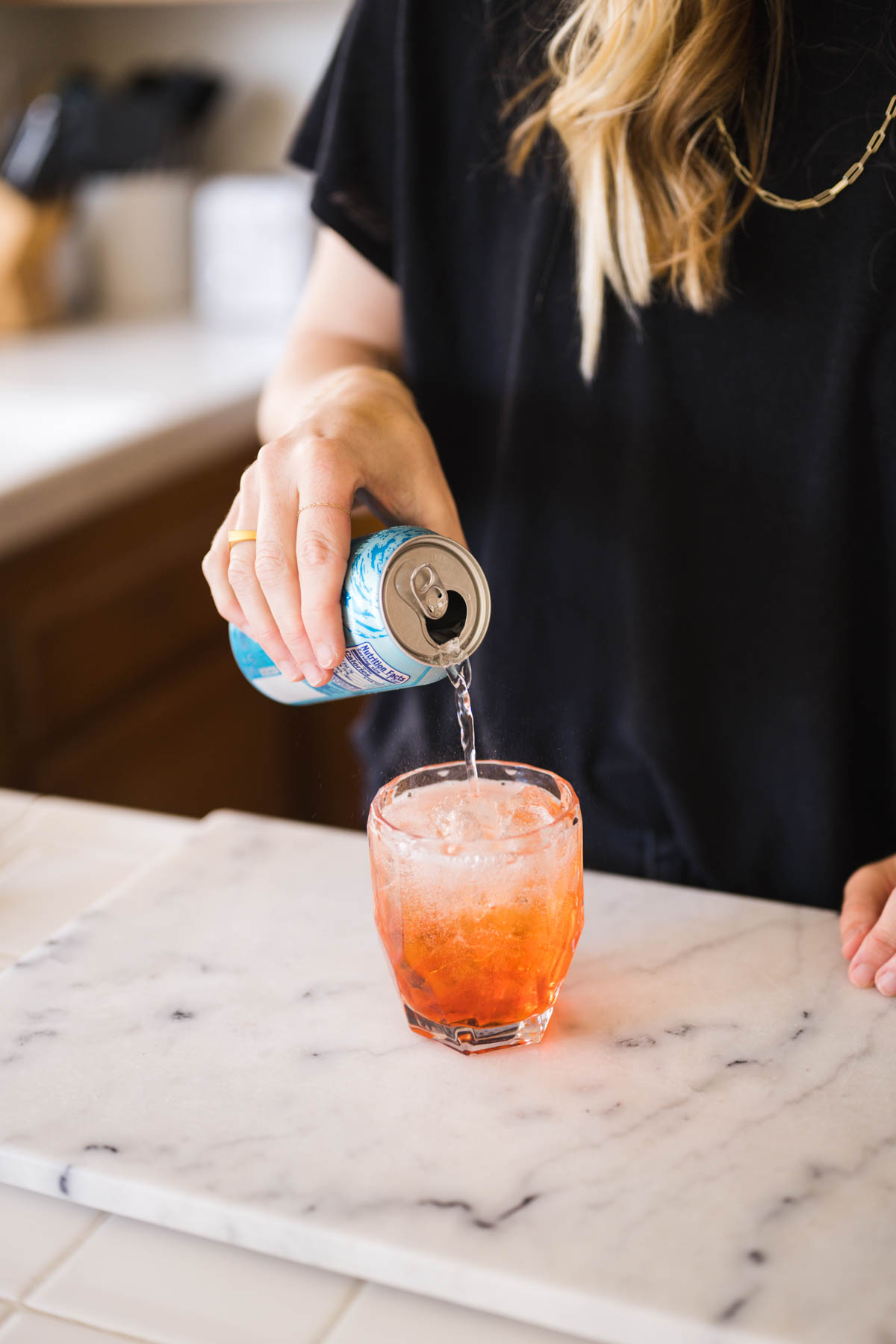 Woman adding club soda to a cocktail glass.
