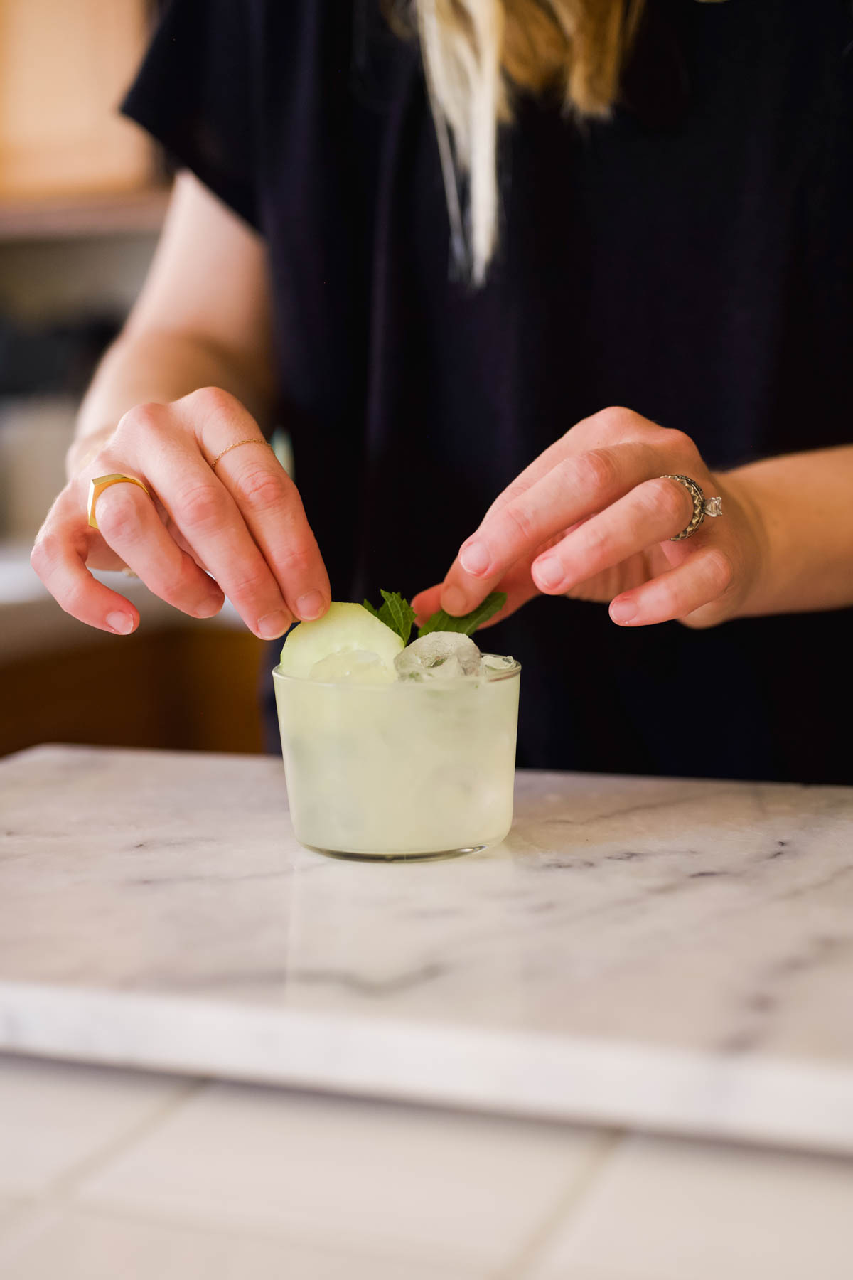 Woman adding a cucumber garnish to a short cocktail glass.