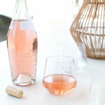 A bottle of rosé on a patio table with a stemless wine glass with rosé next to it.