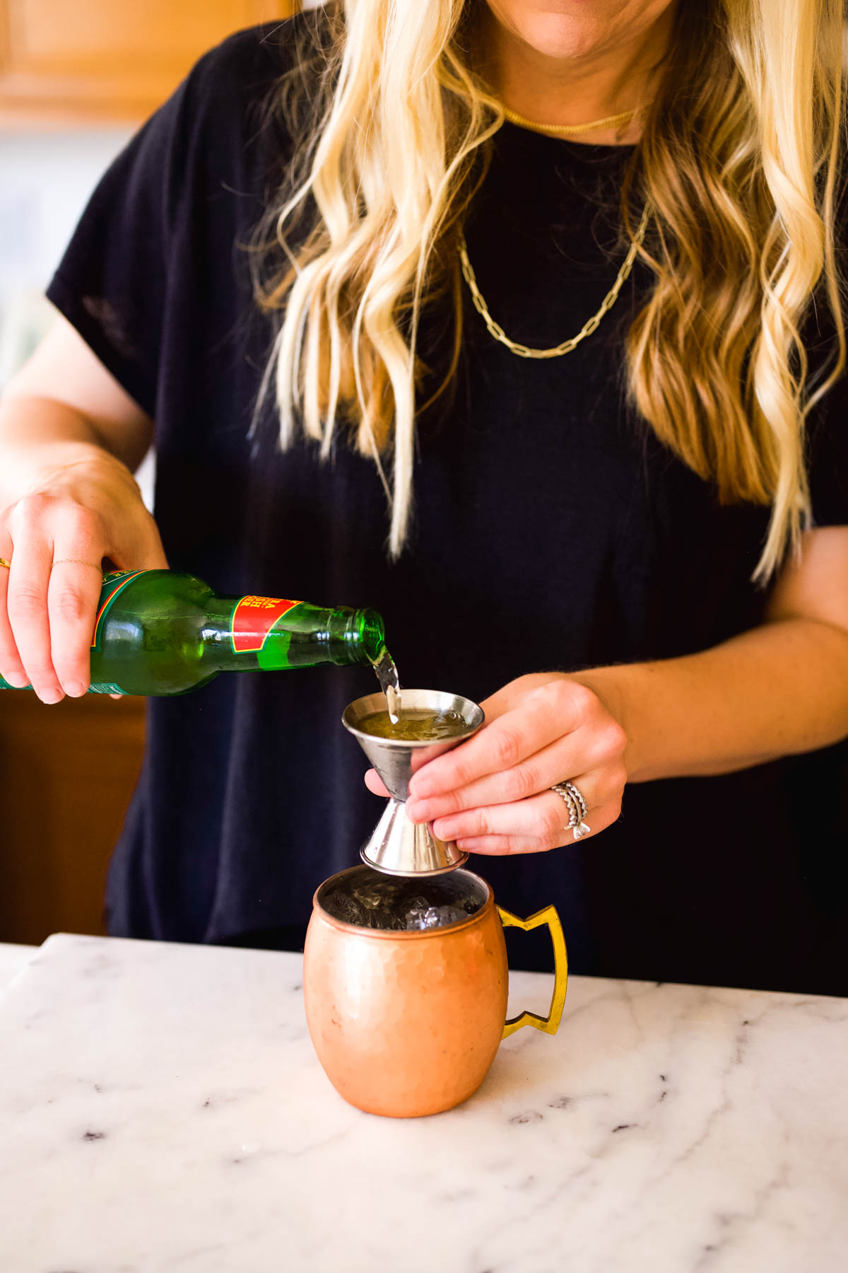 Woman measuring ginger beer in a jigger.