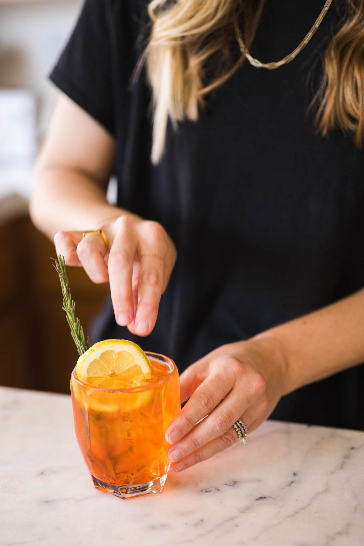 Woman adding lemon slice as a garnish to a cocktail.