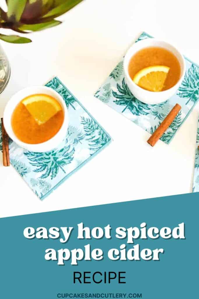 Text: Easy Hot Spiced Apple Cider recipe with 2 small white cups holding hot apple cider with a orange segment and cinnamon sticks on the table next to it.