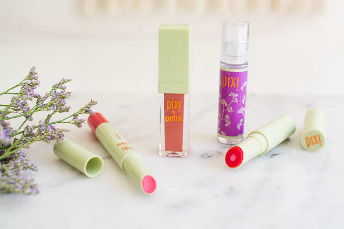 Pixi Cosmetics lip products on a table next to some flowers.