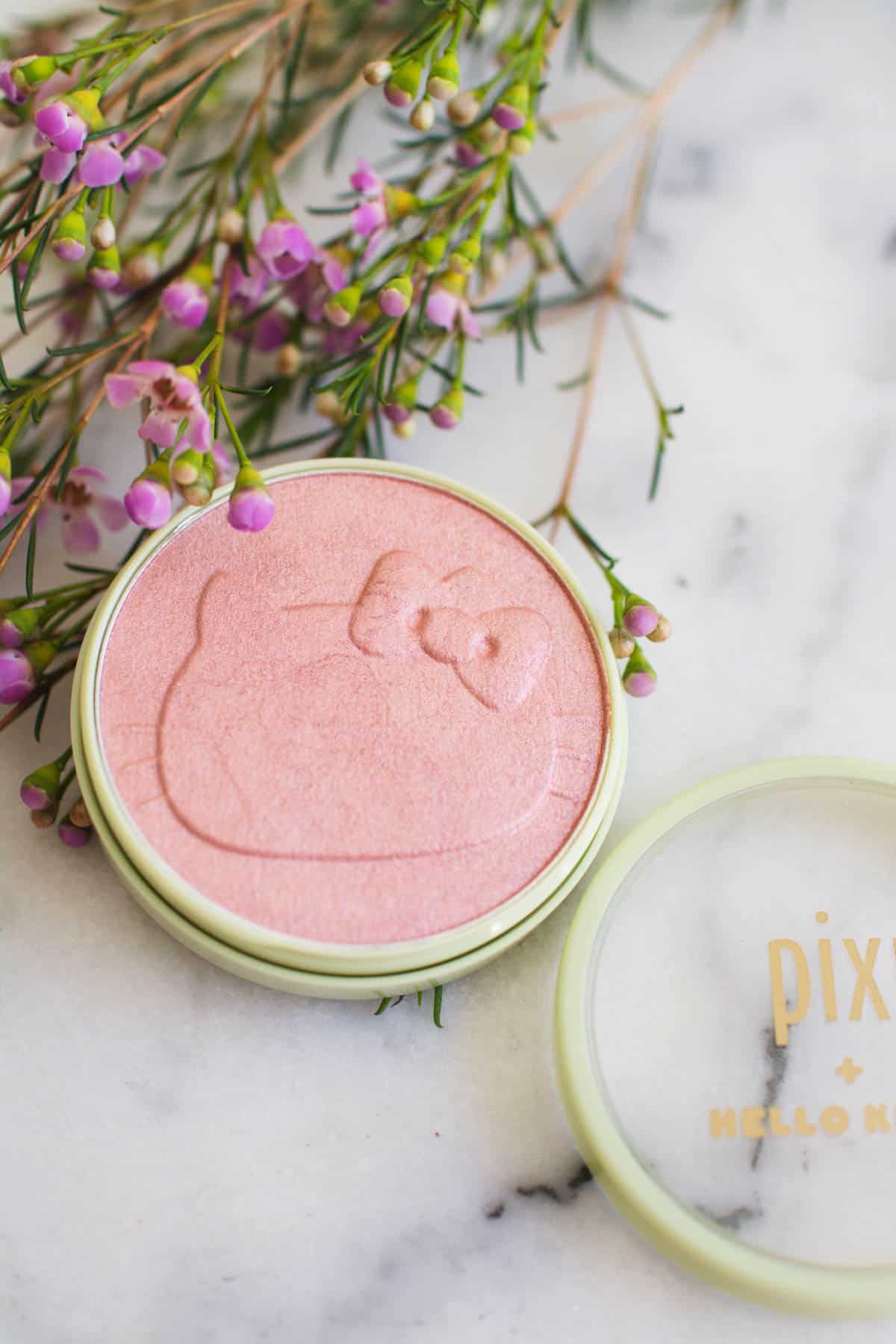 Hello Kitty imprinted blush from Pixi Beauty on a table next to some flowers.