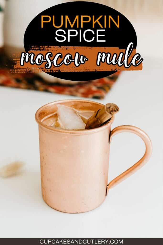 Text: Pumpkin Spice Moscow Mule with a copper mule mug on a white table with a cinnamon stick.