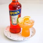 An Aperol Margarita in a stemless margarita glass on a small tray next to a bottle of Aperol.