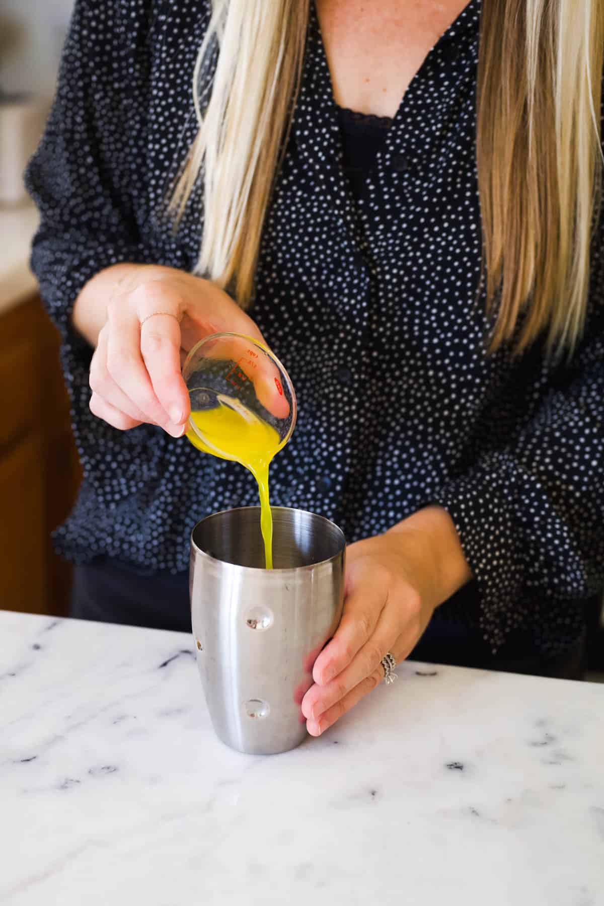 Woman adding fresh orange juice to a cocktail shaker.