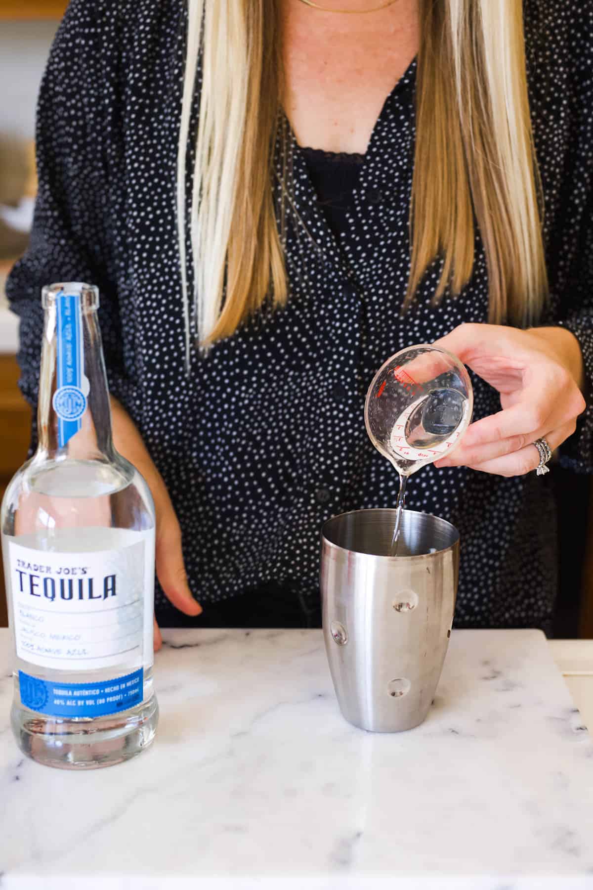 Woman adding tequila to a cocktail shaker.