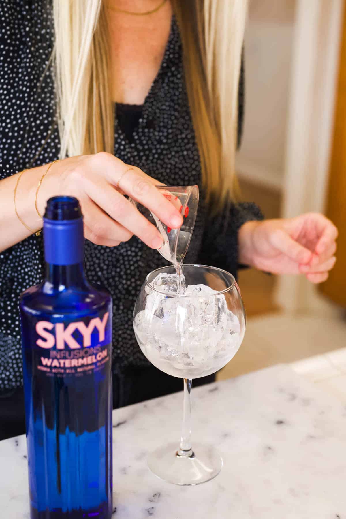 Adding Skyy Watermelon vodka to a wine glass filled with ice.