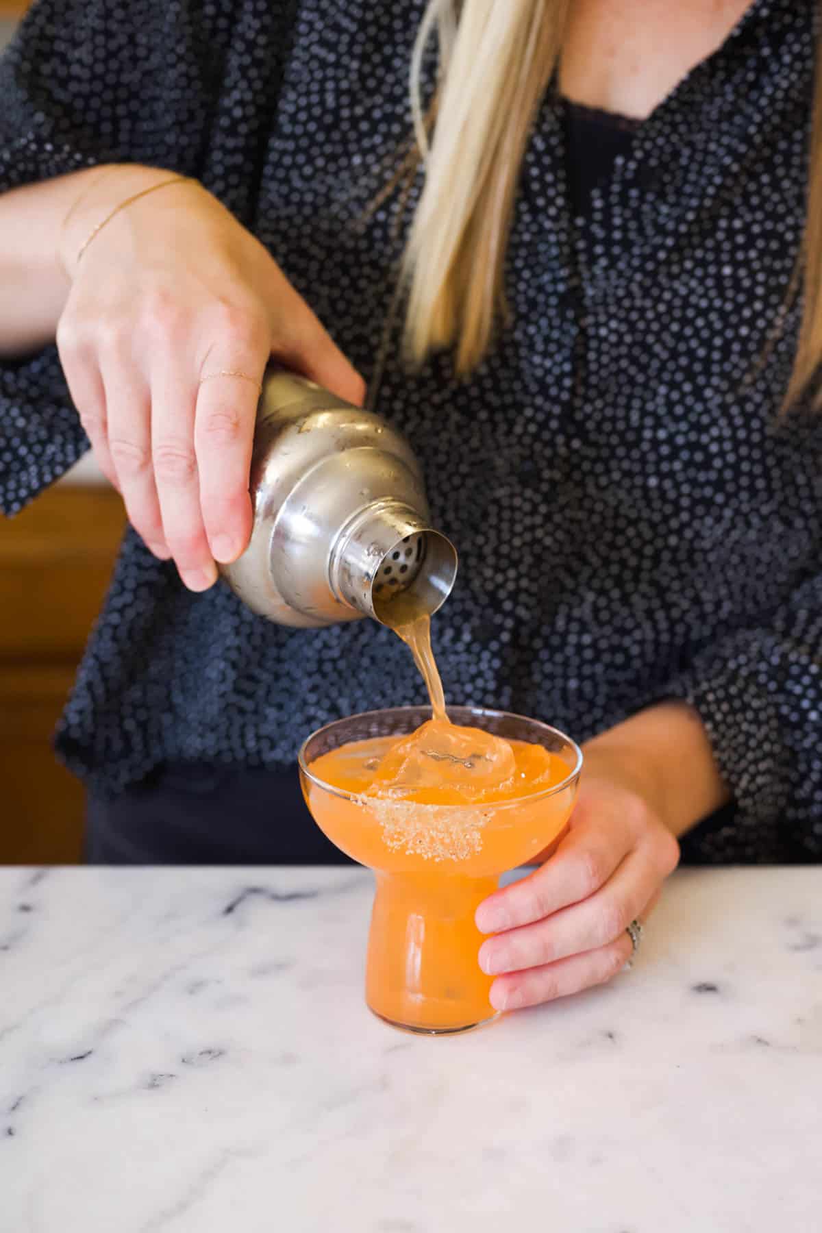 Straining an Aperol Tequila Margarita into a stemless margarita glass.