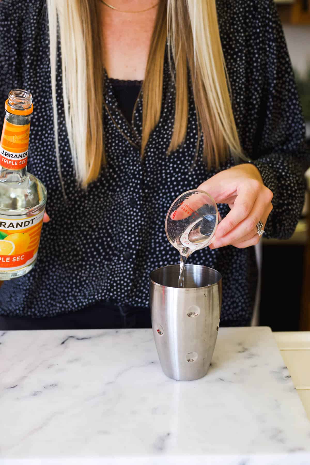 Woman adding triple sec to a cocktail shaker.