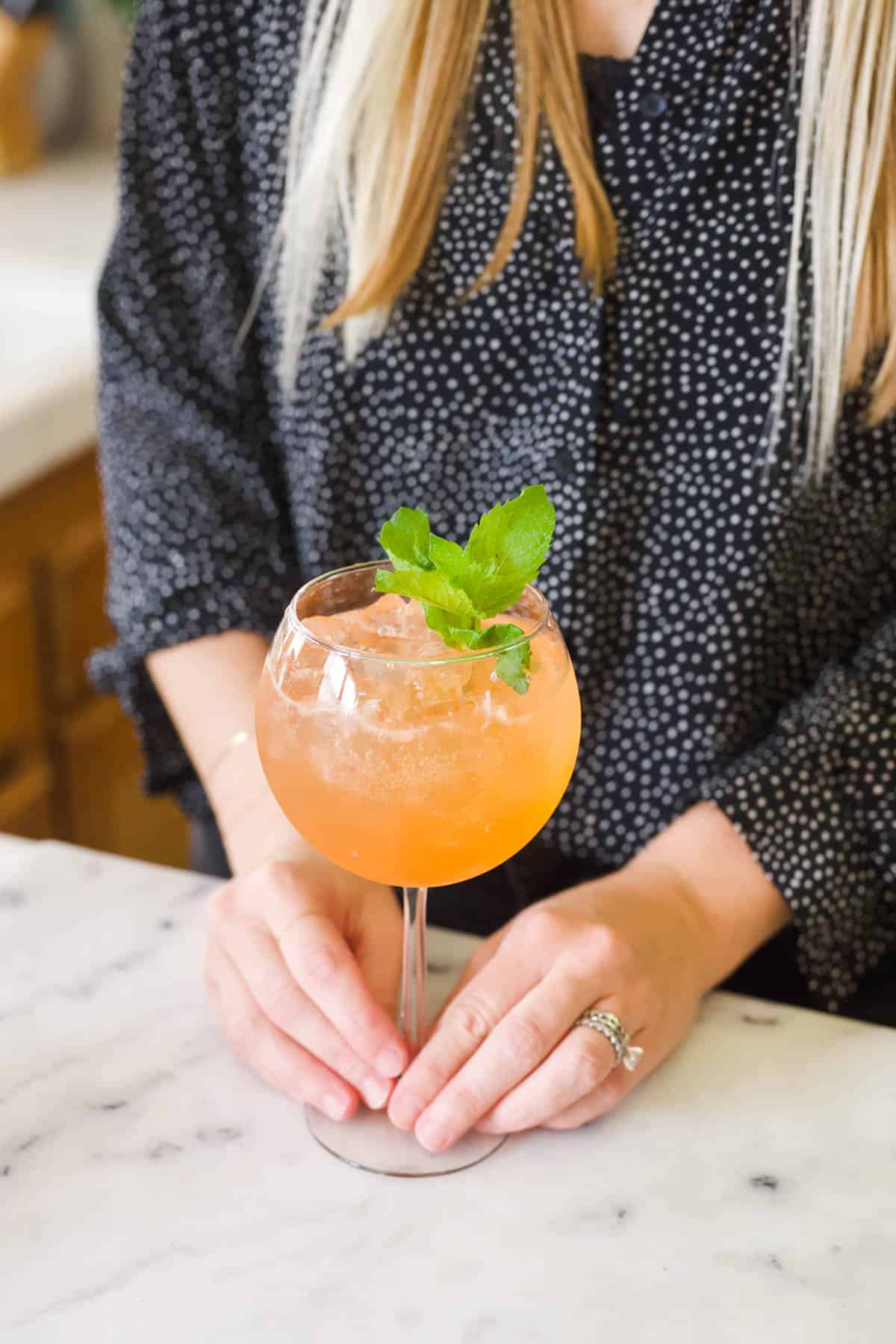 Woman holding a wine glass with a watermelon aperol spritz.