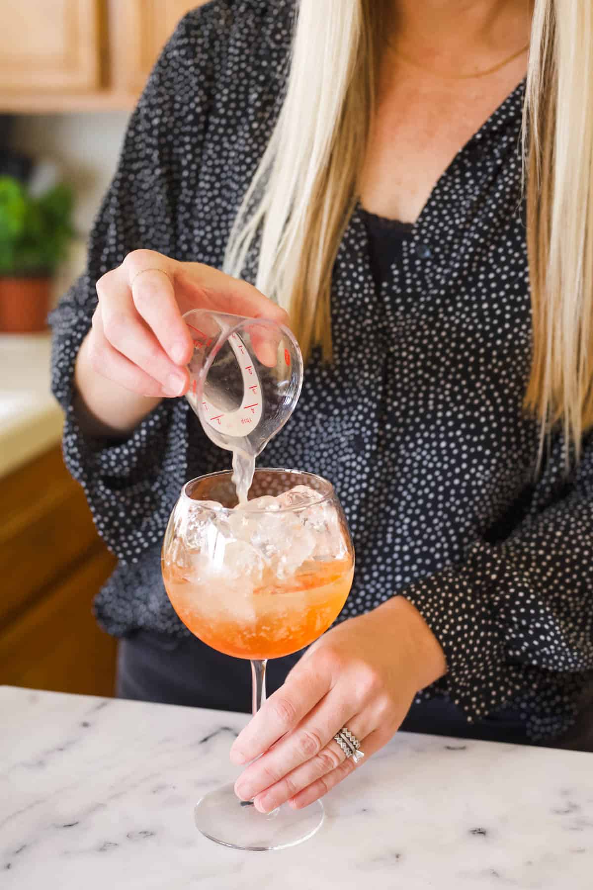 Adding fresh lime juice to a wine glass filled with ice.