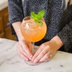 Woman touching the stem of a wine glass with a watermelon cocktail.