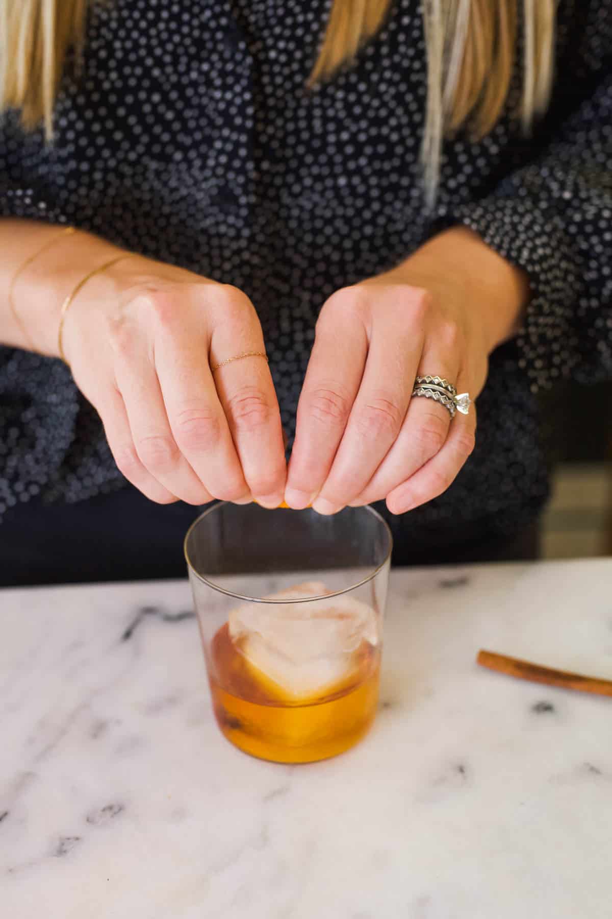 Woman squeezing an orange peel over the top of a Fireball Old Fashioned.