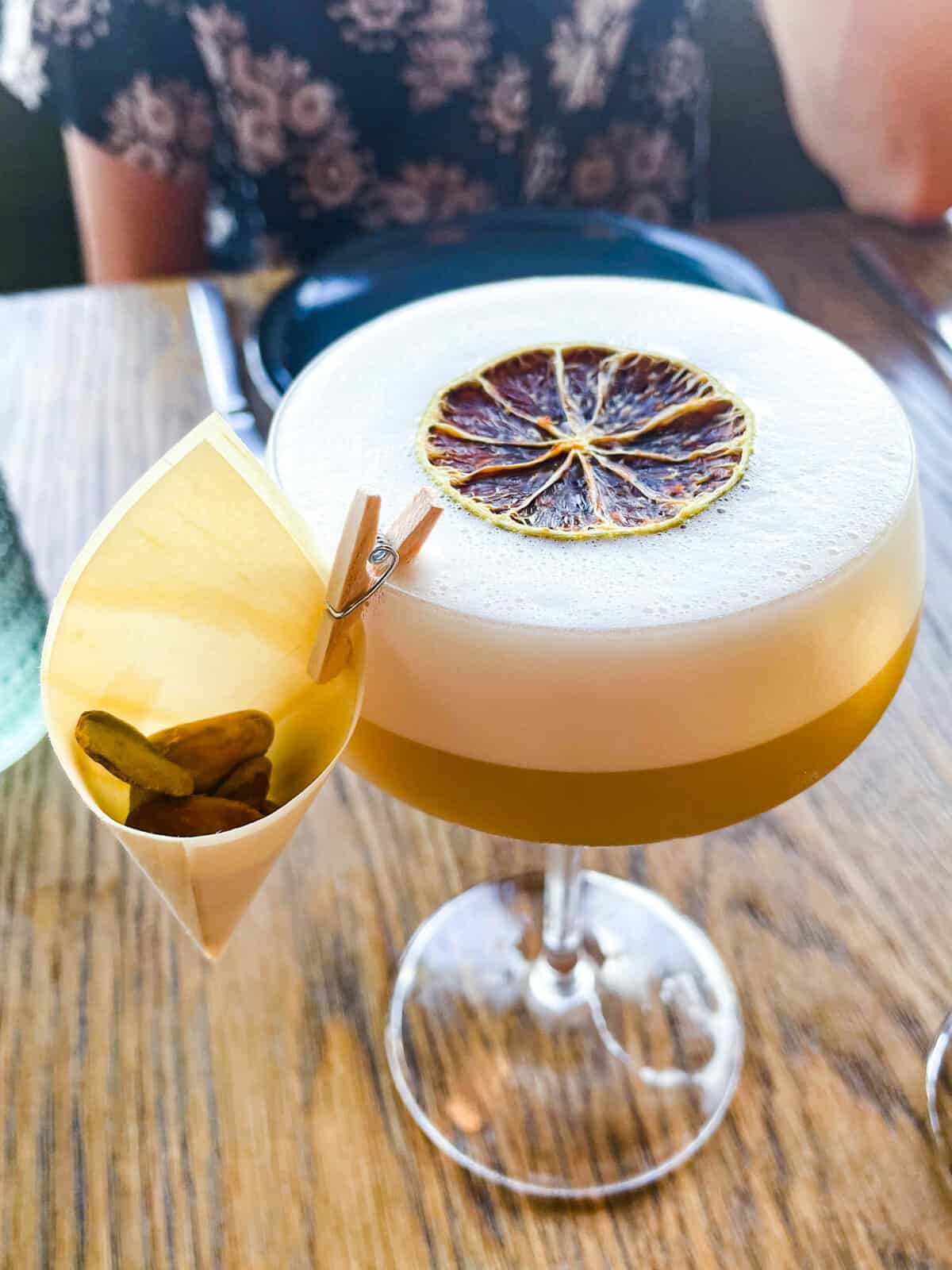 Garnish clipped to a glass with a mini clothespin holding on a small cup with nuts in it.