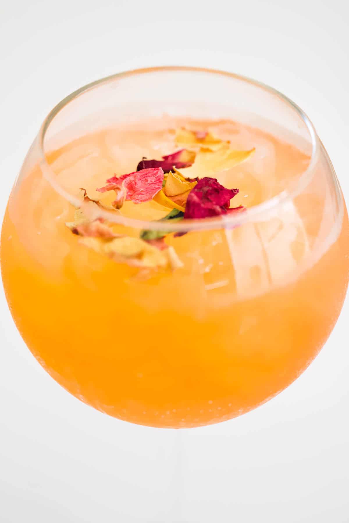 Dried flower petals floating on the top of a cocktail in a spritz glass.