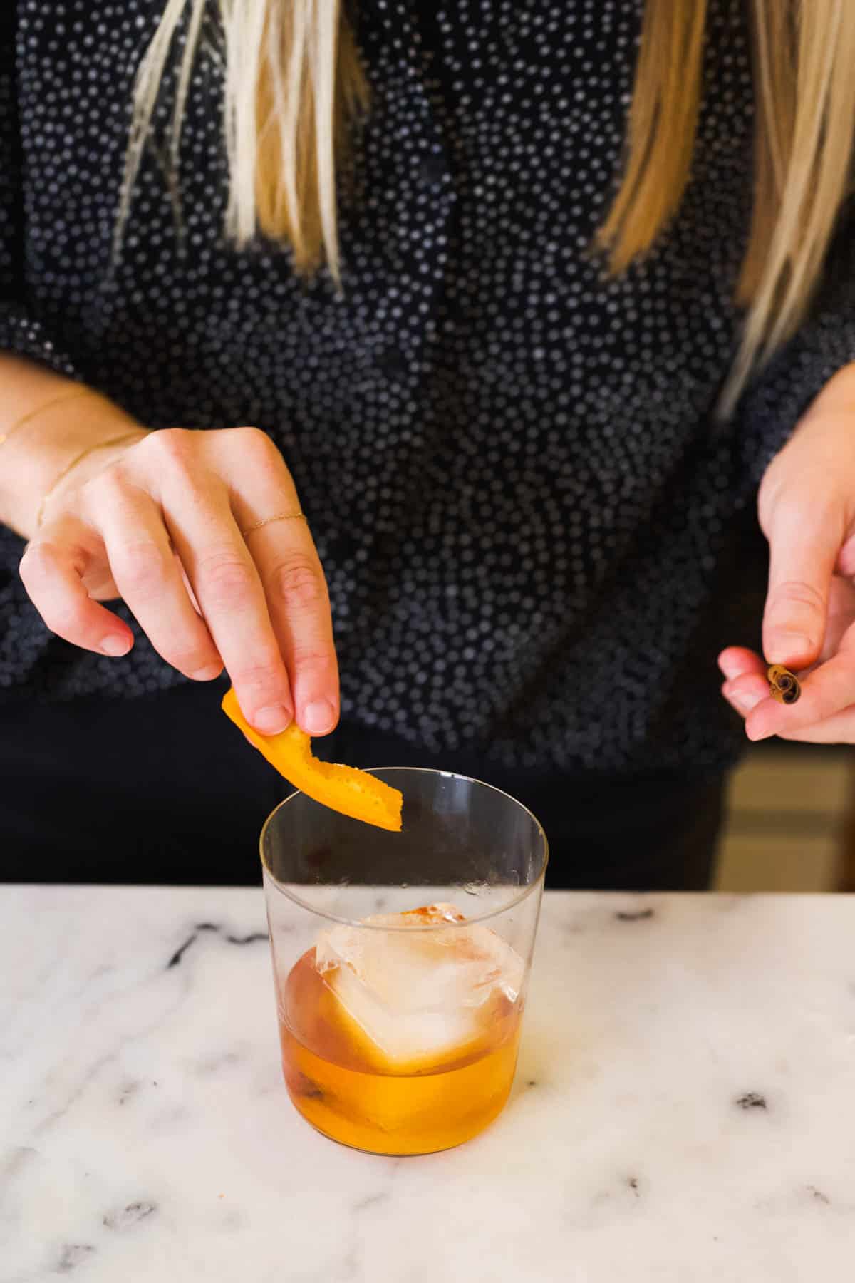 A woman rubbing an orange peel on the rim of a cocktail glass.