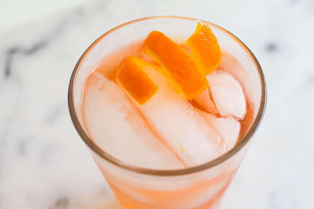 A drink with an orange peel citrus twist on top of it.