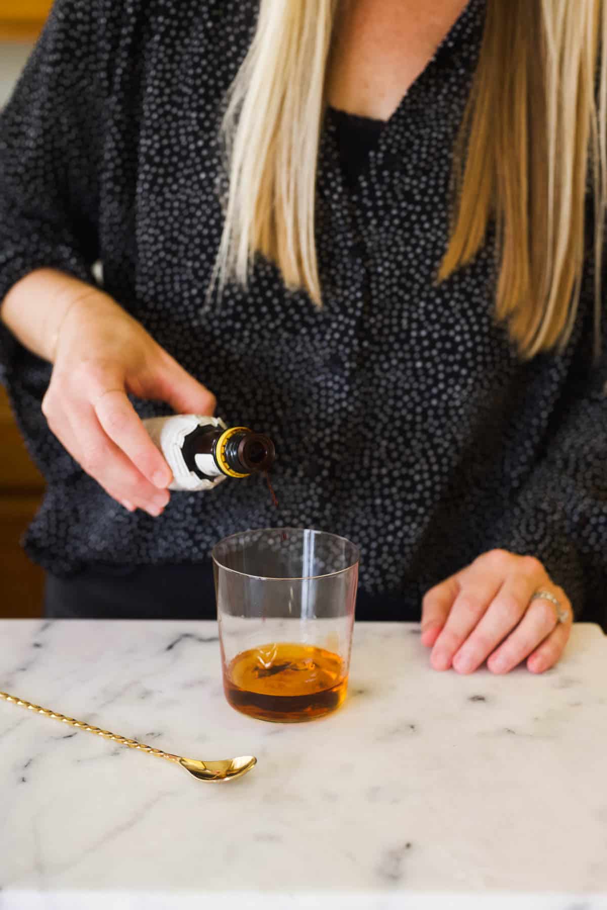 Woman adding bitters to a Fireball Old Fashioned.