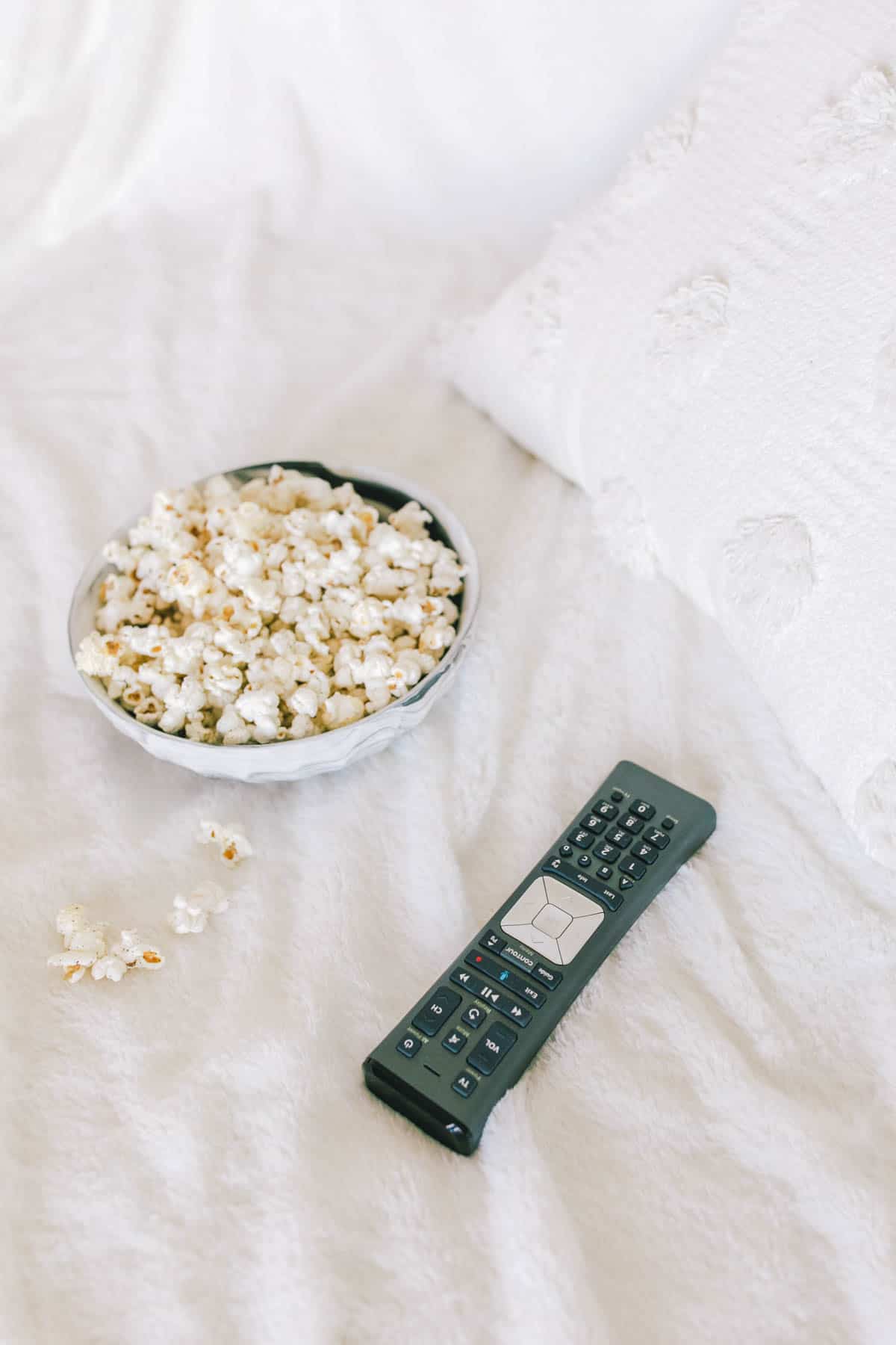 A TV remote and a bowl of popcorn on the couch.