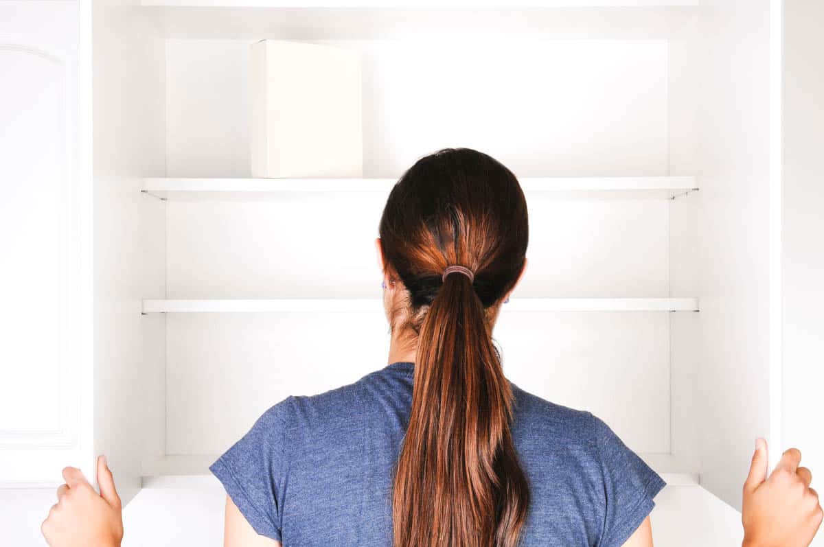 Woman looking in an empty food cabinet.