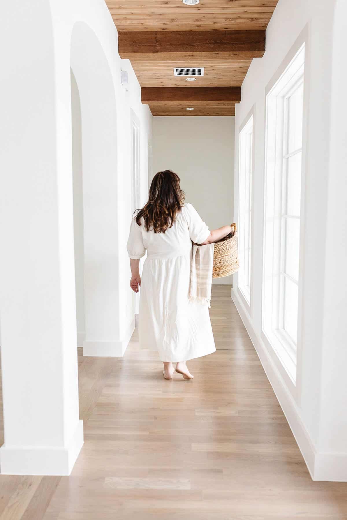 Woman carrying a laundry basket down a hallway.