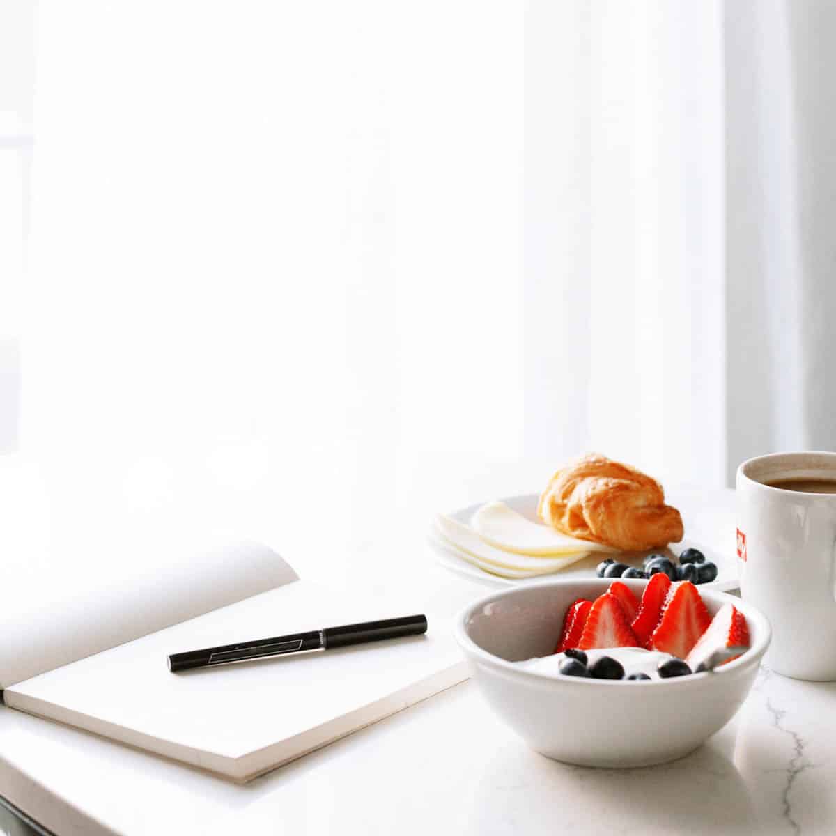 A notepad and pen used for meal planning on a table next to breakfast items.