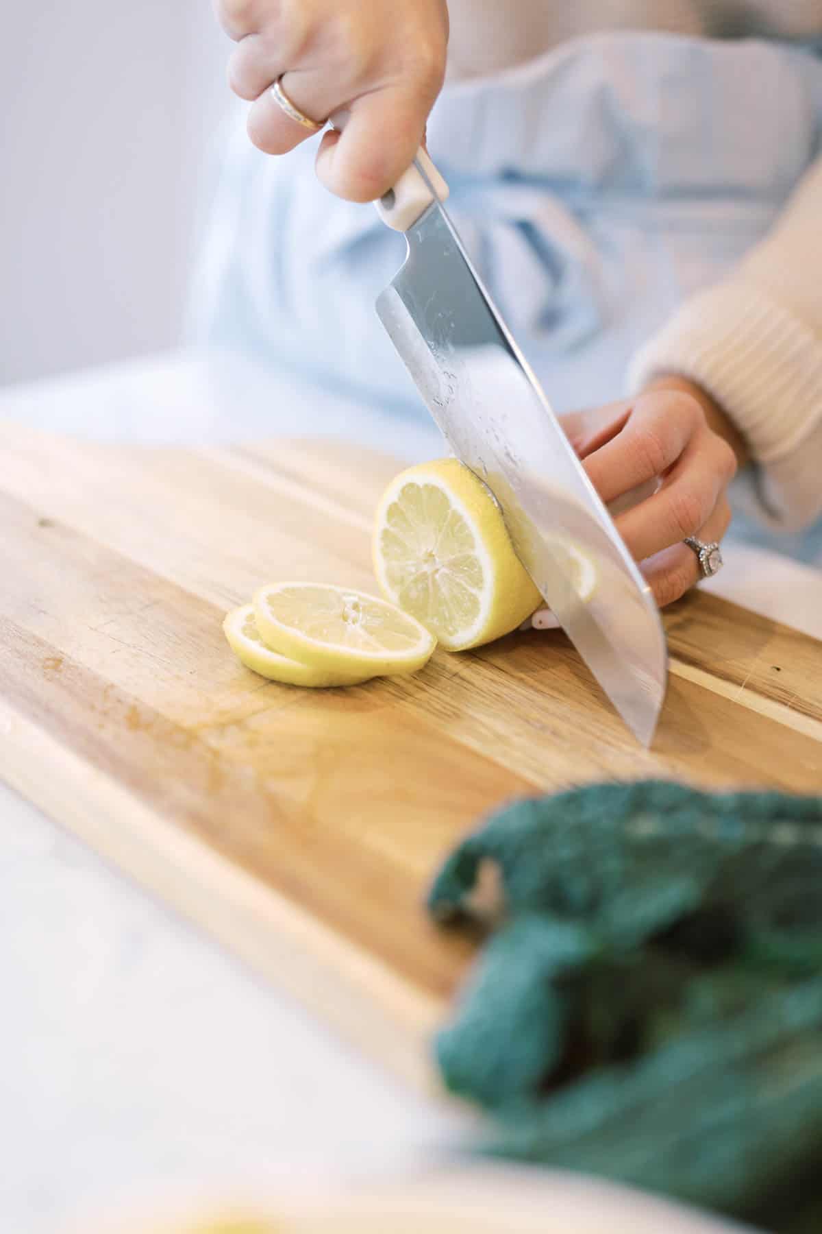 Woman cutting a lemon on a cutting board next to kale.
