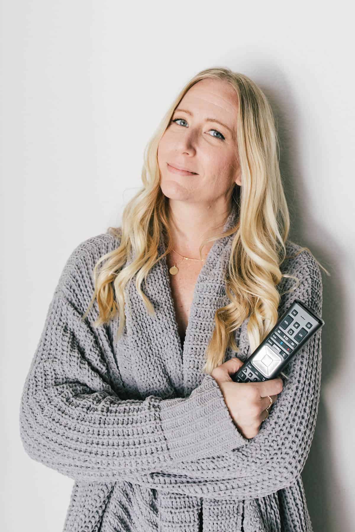 A mom in a cozy sweater holding a remote.