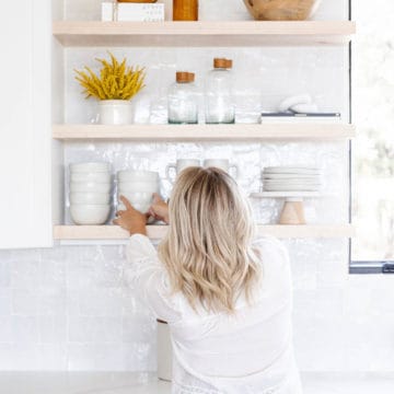 A woman clearing the clutter by putting dishes away.