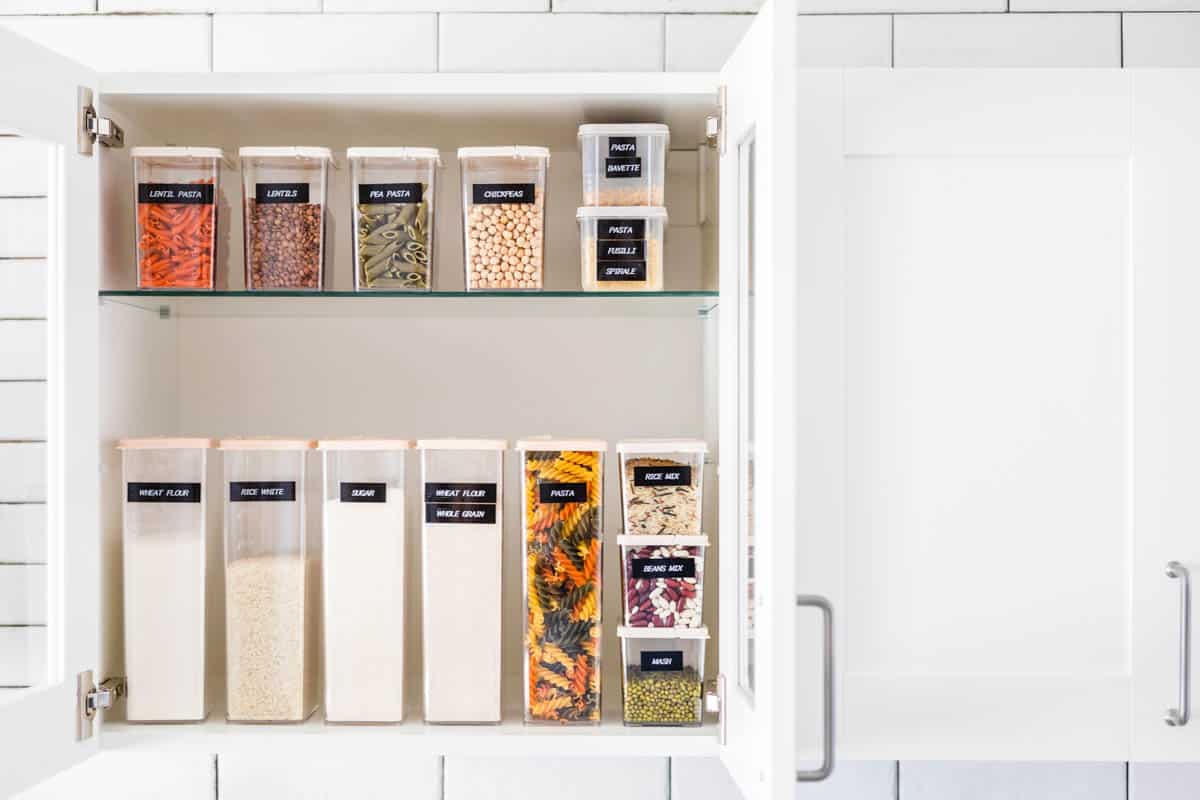 An organized food cabinet with labeled containers. 