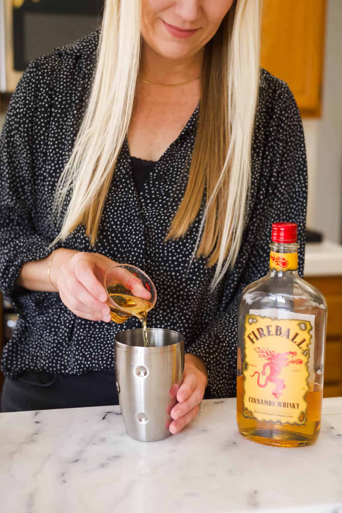 Woman adding Fireball whisky to a cocktail shaker.