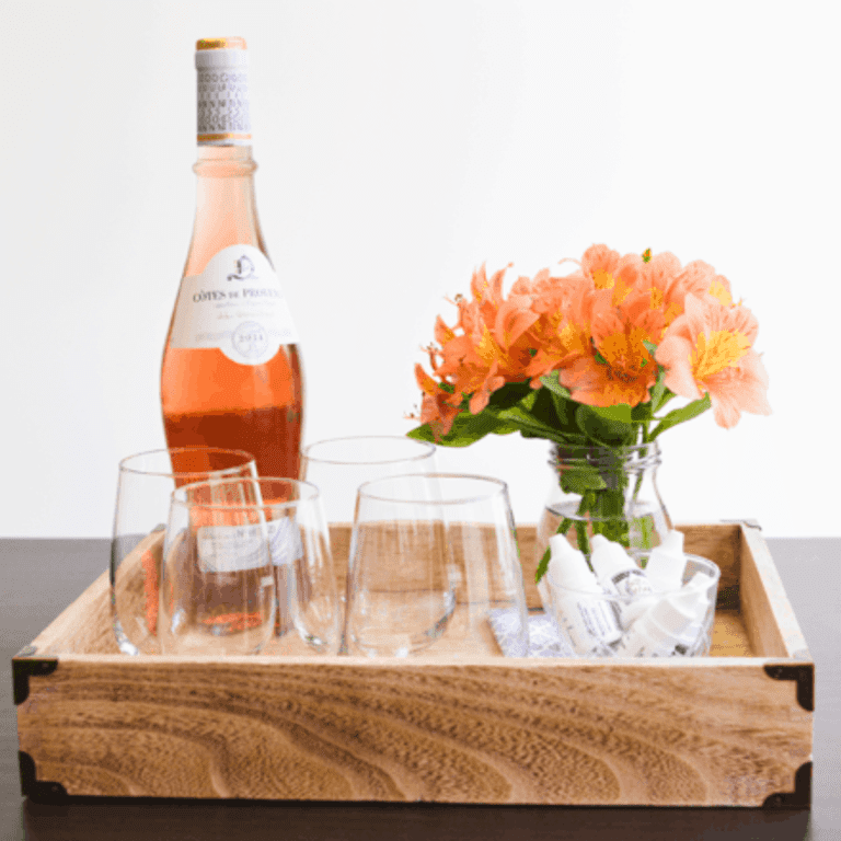 A wooden tray on a table with stemless wine glasses, a bottle of rose and flowers.