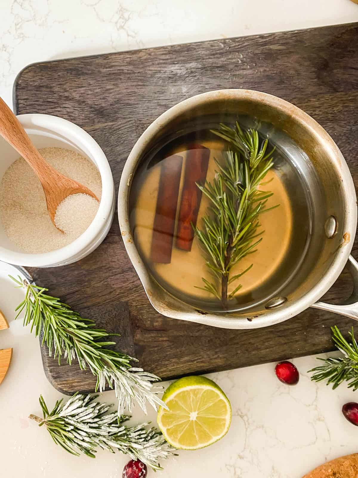 A saucepan with cinnamon sticks and rosemary to make a simple syrup.