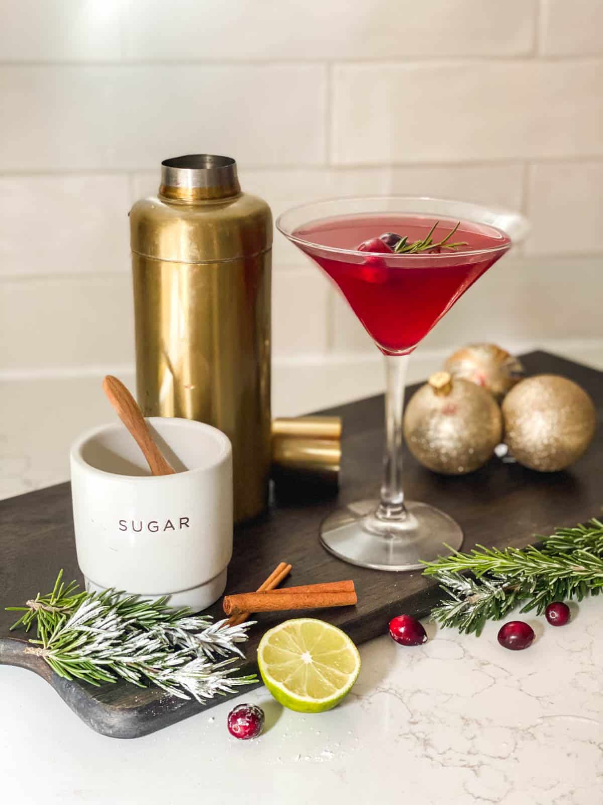 A holiday cosmo in a martini glass next to ingredients for the drink. 