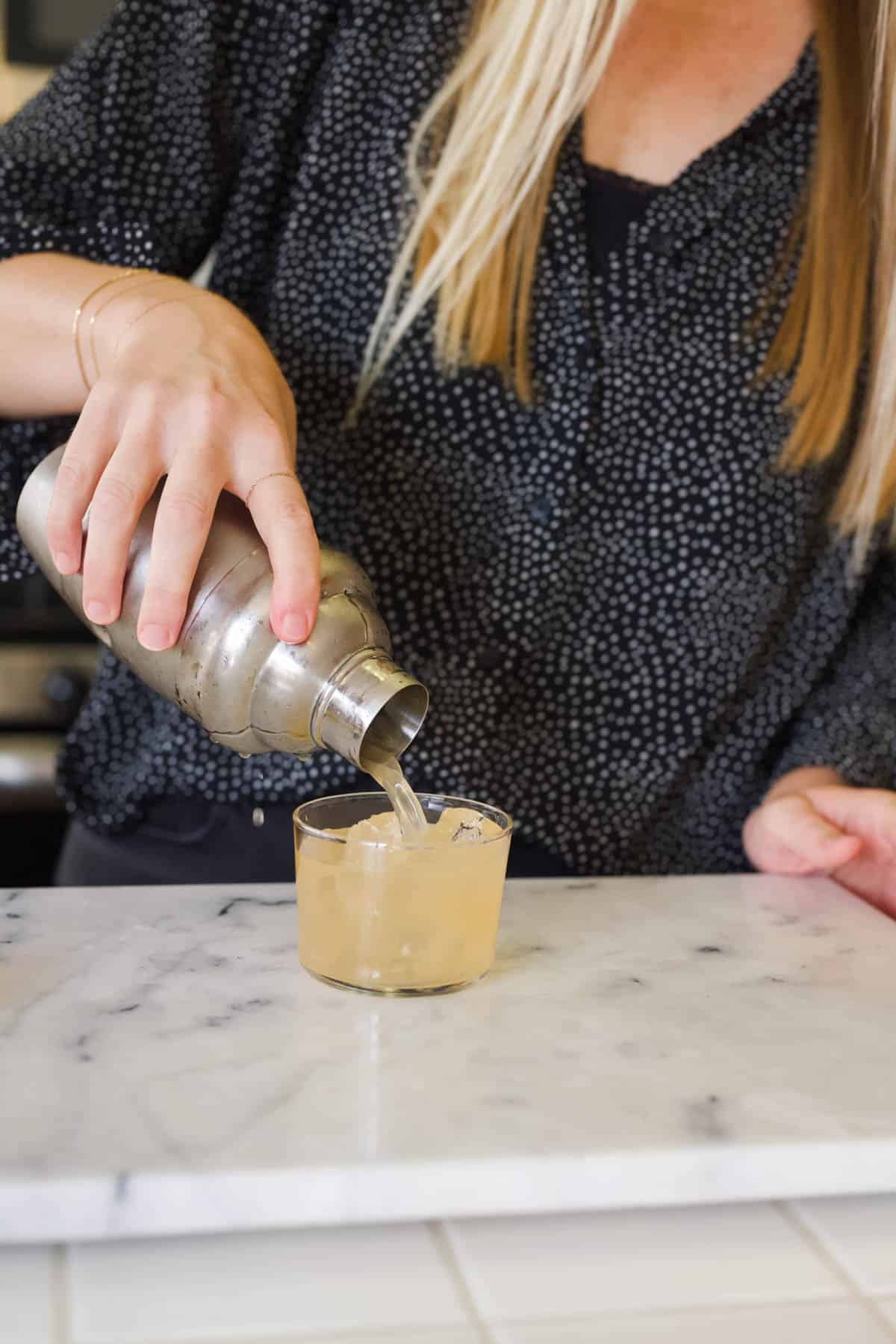 Woman pouring a Fireball Sour cocktail into a short cocktail glass.