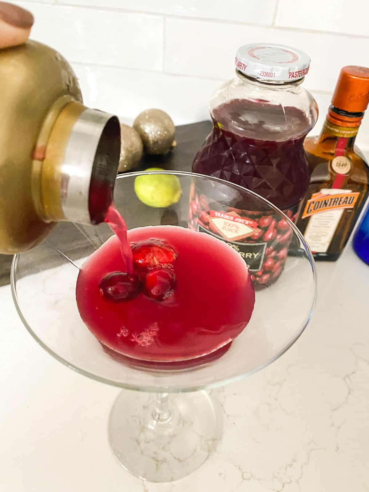 A red cocktail being poured into a martini glass.