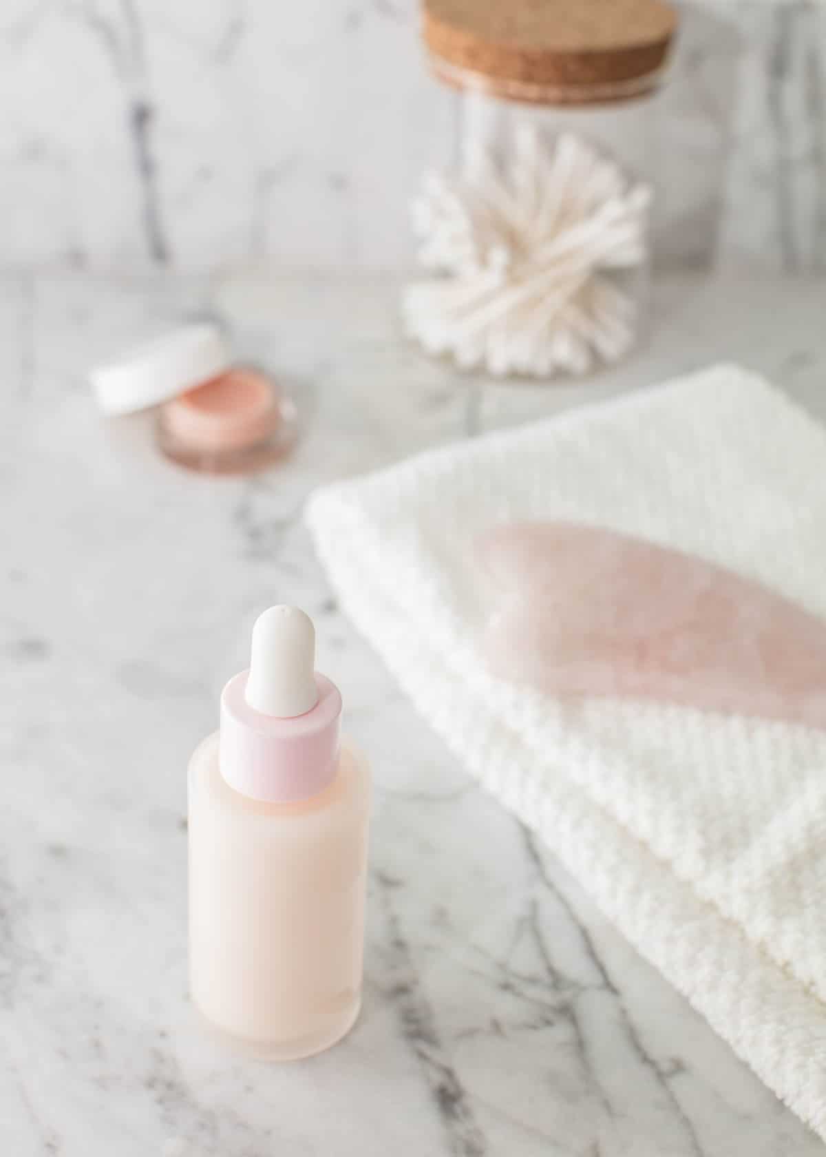 Pink bottle on a marble counter next to other beauty products.