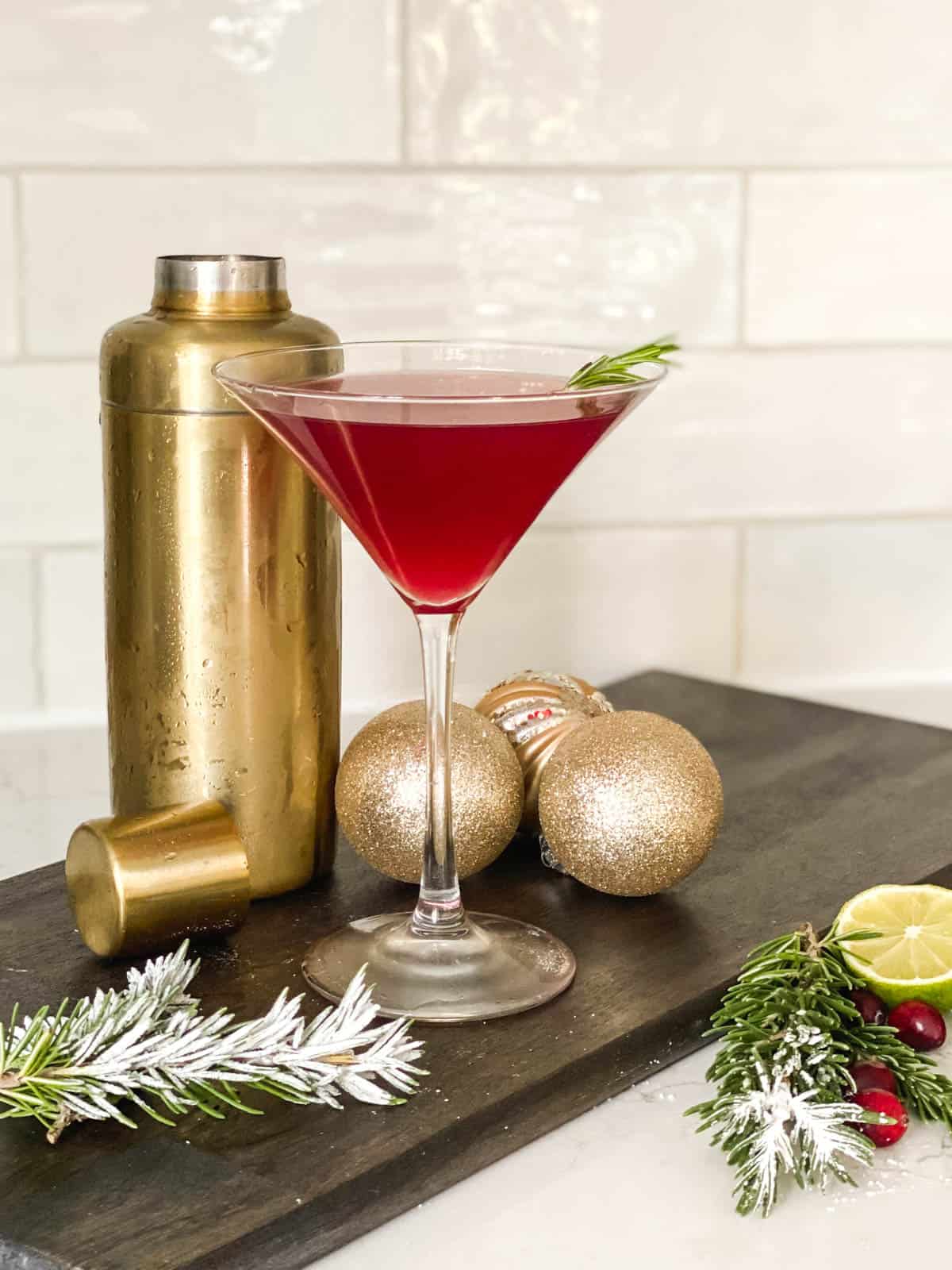 A cosmopolitan for Christmas in a martini glass next to a gold cocktail shaker.