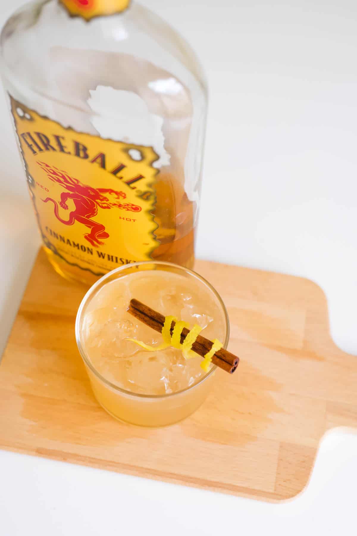 A bottle of fireball behind a Cinnamon sour in a cocktail glass with cinnamon stick garnish.
