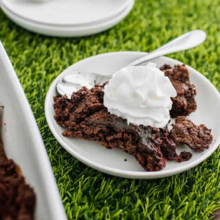 A portion of chocolate dump cake topped with whipped cream and served on a small white dessert plate.